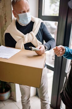 Senior man with facemask receiving a package and making payment indoors.
