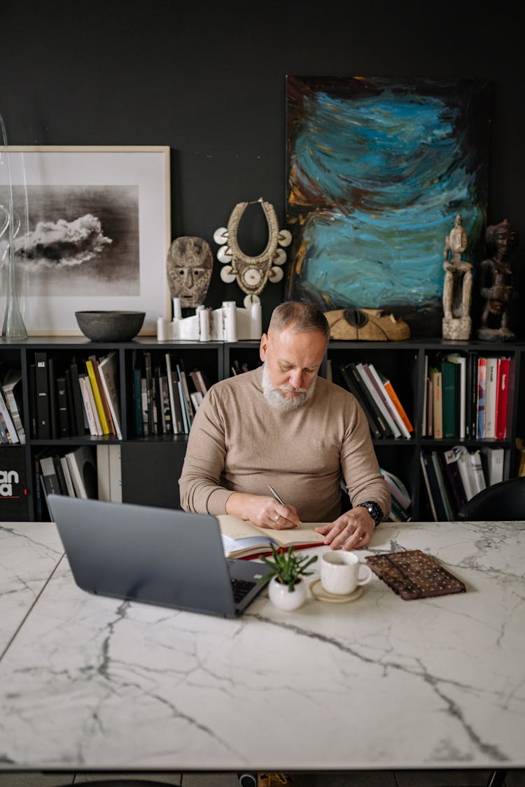 An Elderly Man Busy Writing On A Notebook