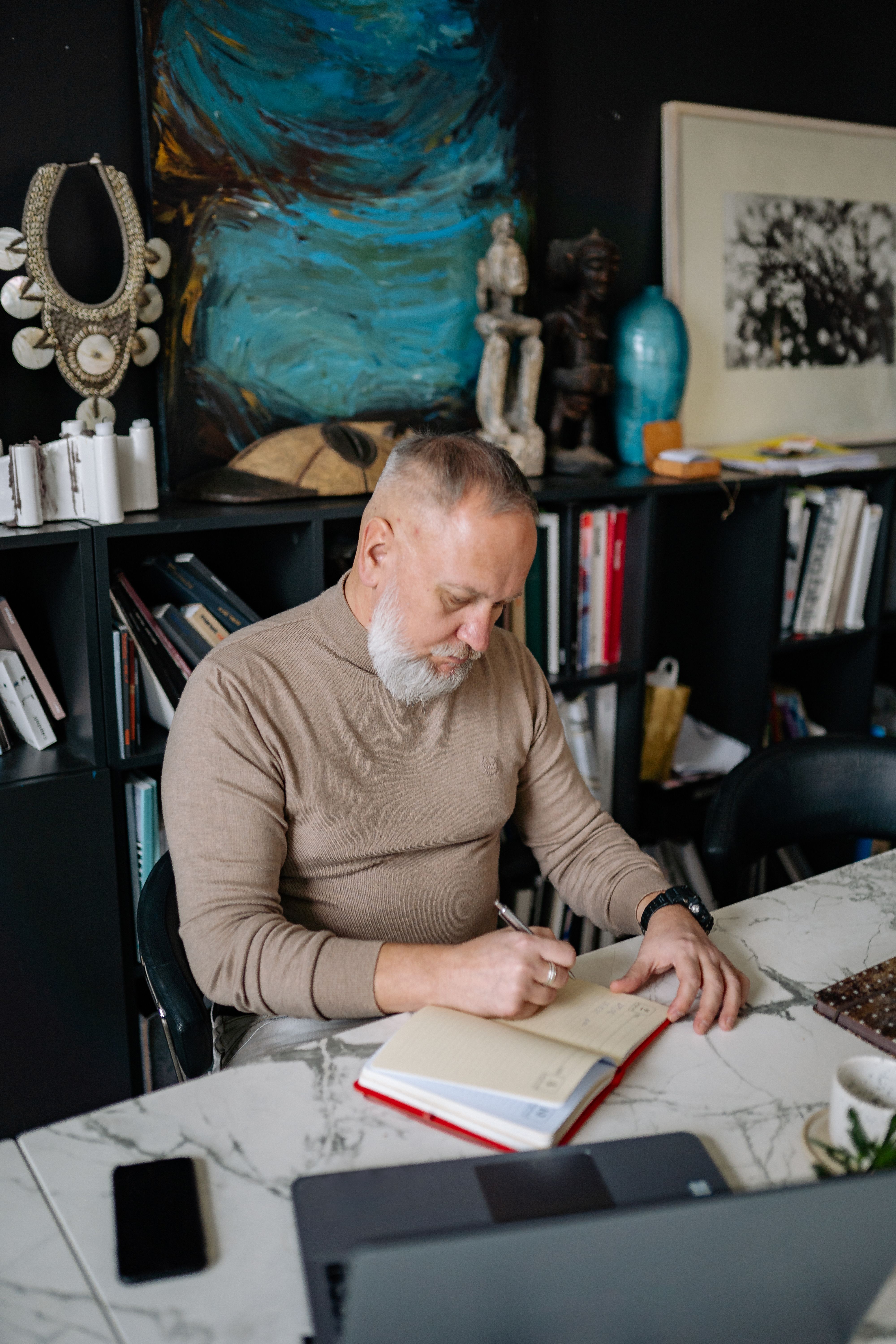 A senior man writes in a notebook at a stylish home office, enhancing productivity.