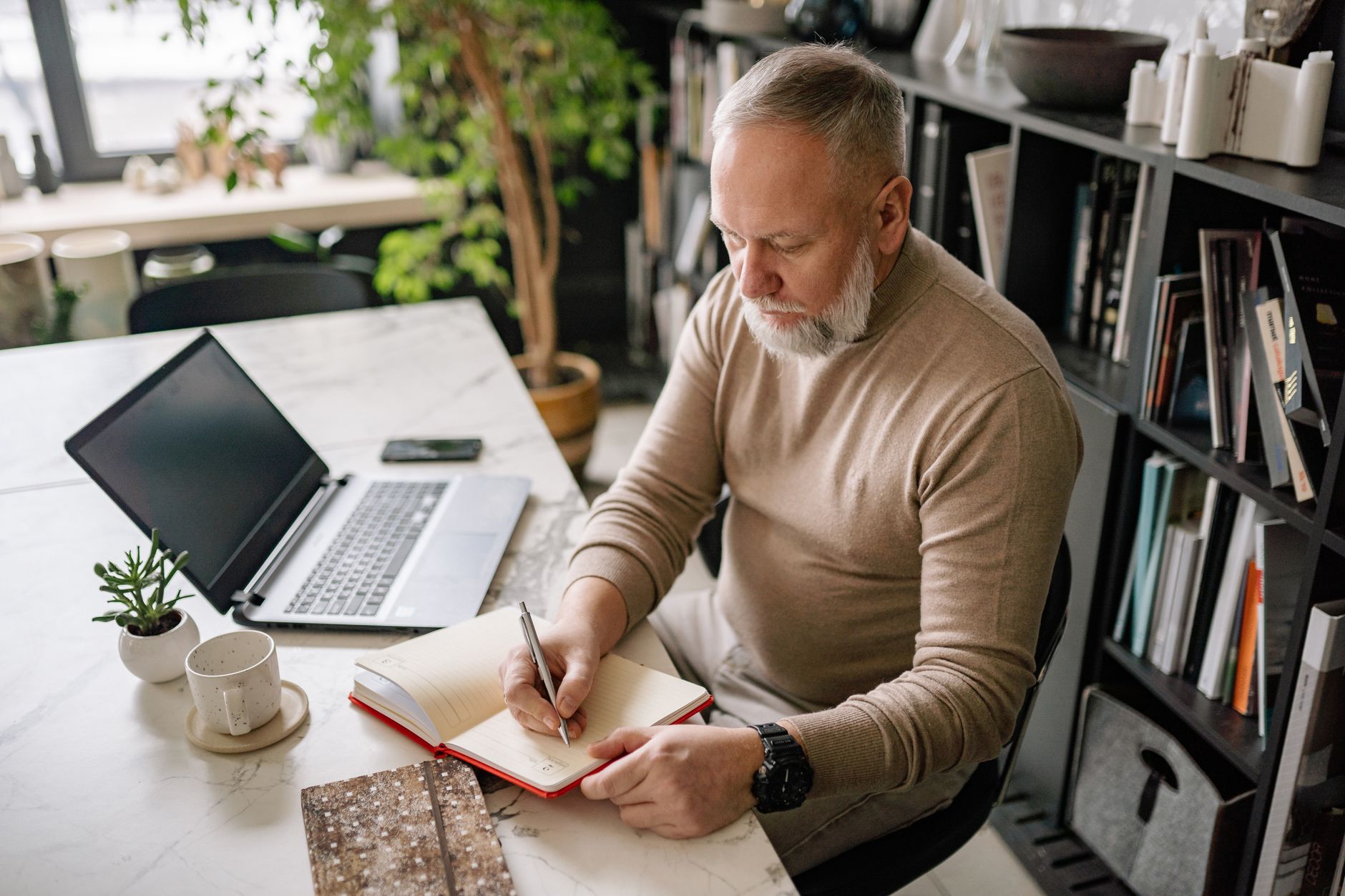A coach working at a tidy home office desk with a laptop and an open notebook