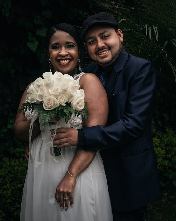 Portrait Of Smiling Newlyweds With Flowers Bouquet