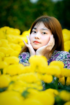 A serene portrait of a young woman posing amidst bright yellow flowers, exuding calm and beauty.