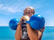 在阳光明媚的日子里，运动员在海边举起蓝色壶铃，展示力量与健身成果