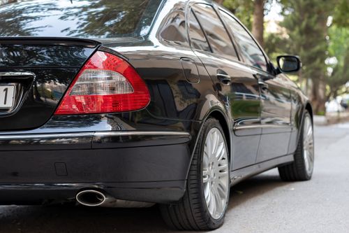 Free Close-up of a gleaming black car parked on a tree-lined city street. Stock Photo