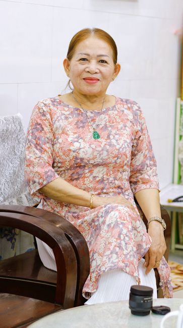 Portrait of an elderly Asian woman sitting and smiling indoors with a floral dress.