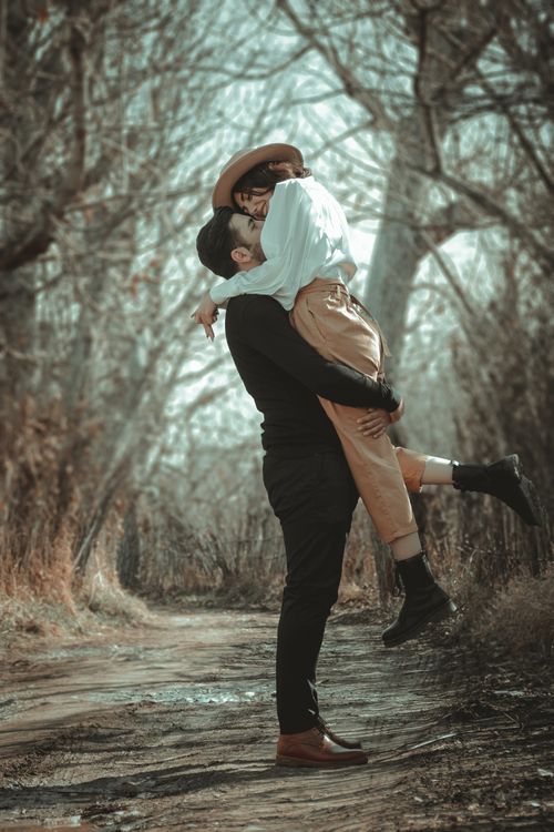Free A couple embracing in a romantic outdoor setting amidst a serene woodland backdrop, capturing a moment of affection. Stock Photo