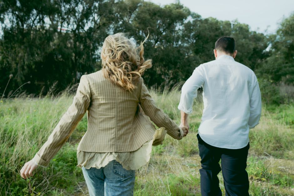 Couple holding hands walking through a lush field, showcasing natural outdoor affection.