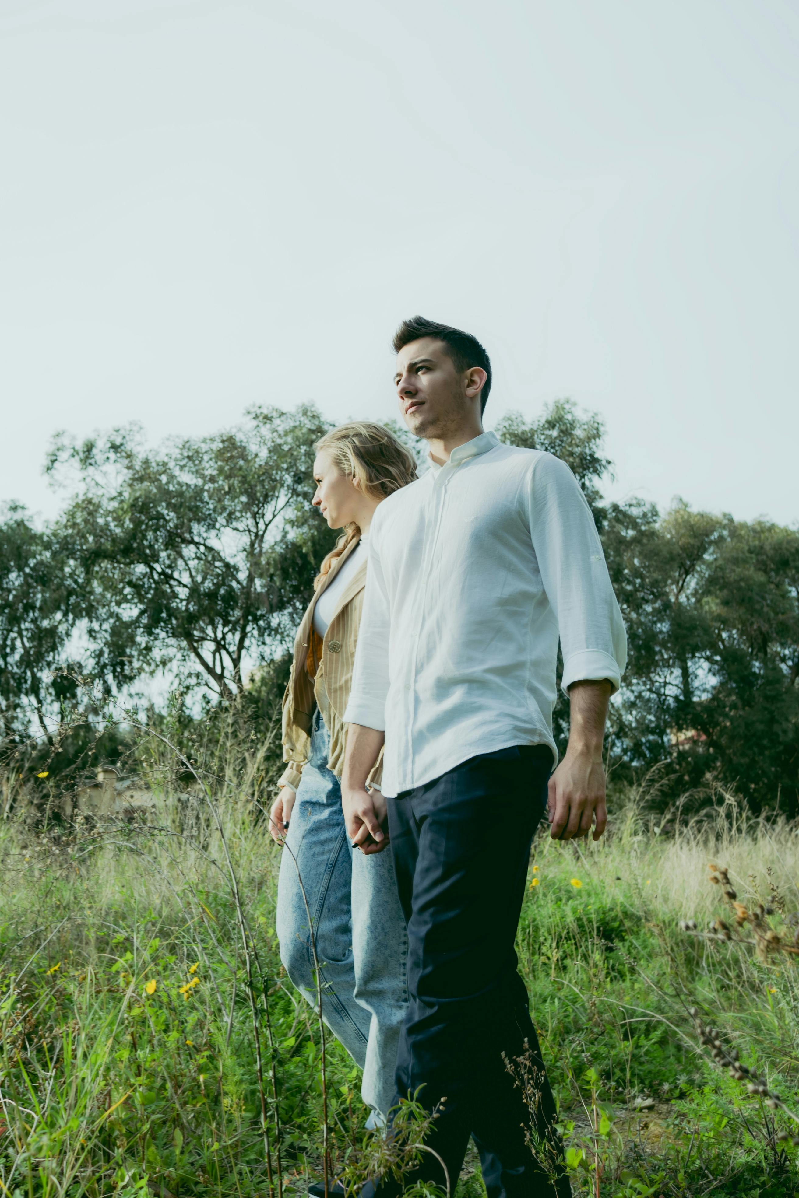 A couple holding hands while taking a walk in a lush green outdoor setting.