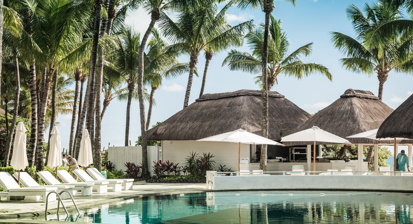 A tropical resort swimming pool lined with palm trees and loungers