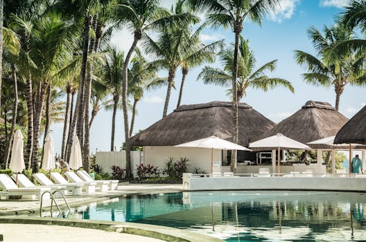 Relax by the pool at a tropical resort with palm trees and thatched huts, epitomizing a summer getaway.