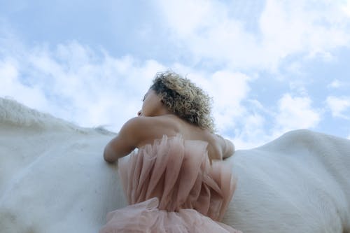 Low Angle Shot of a Person in a Stylish Dress Leaning on a White Horse