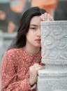 A Woman Peeking Behind the Concrete Statue while Looking at the Camera