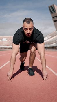 Focused young male athlete at starting line on outdoor track, ready to sprint.
