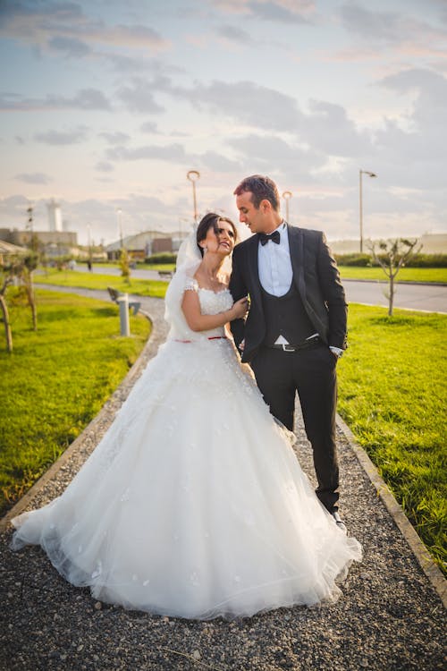 Man in Black Suit and Woman in White Wedding Dress Standing near the Green Grass Field 