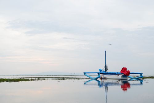 Free Tranquil boat floating on serene waters in Bali, Indonesia, under a cloudy sky. Stock Photo