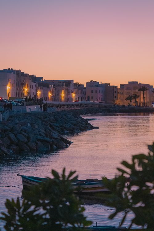 Free Charming coastal town at sunset. Houses light up the waterfront with a pink and orange sky. Stock Photo