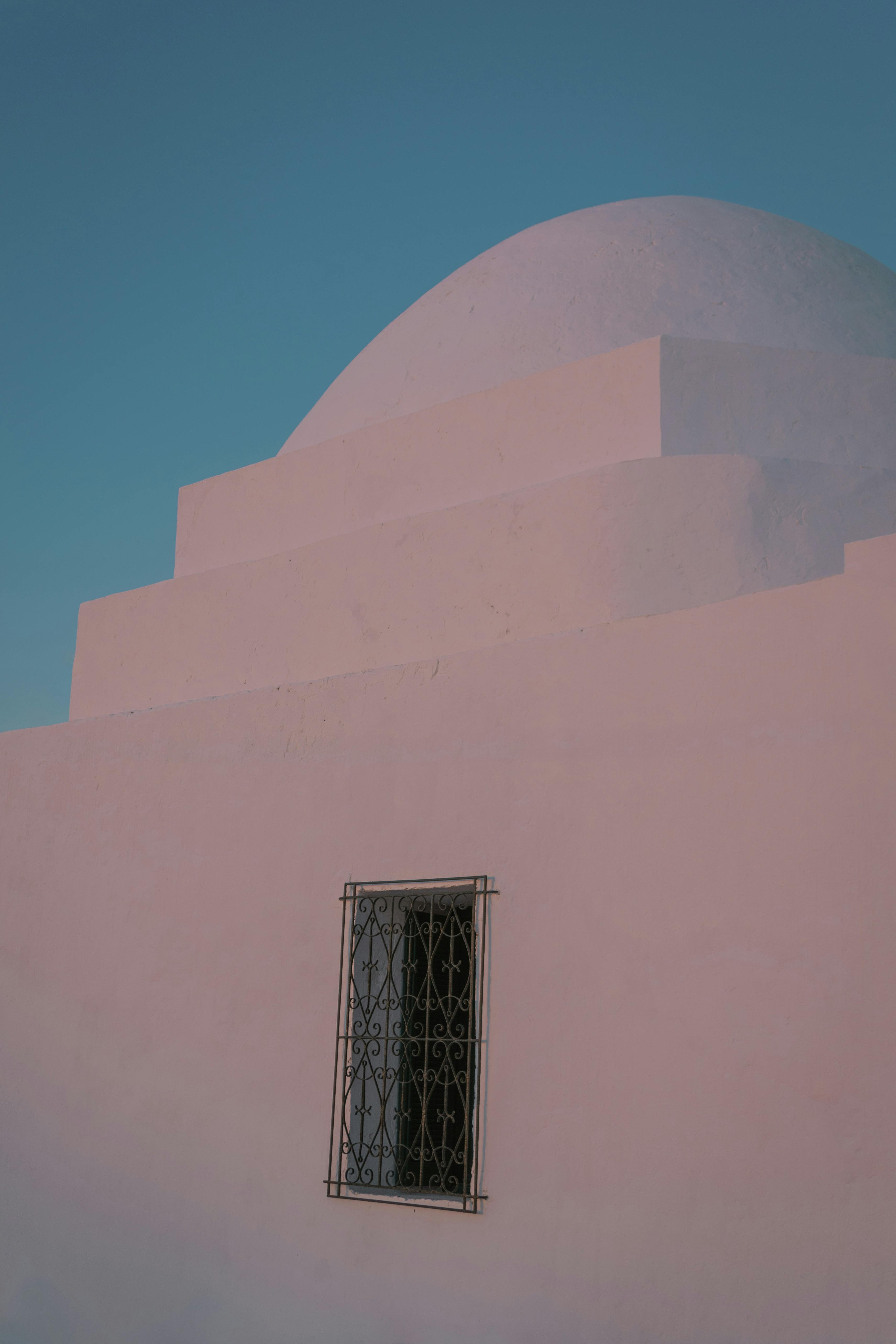 Beautiful minimalist architecture featuring a white dome and metal window against a clear sky.