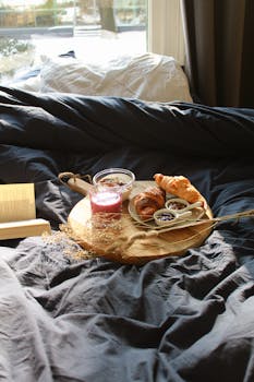 A warm breakfast setting on a bed with croissants, yogurt, and smoothie, perfect for a lazy morning.
