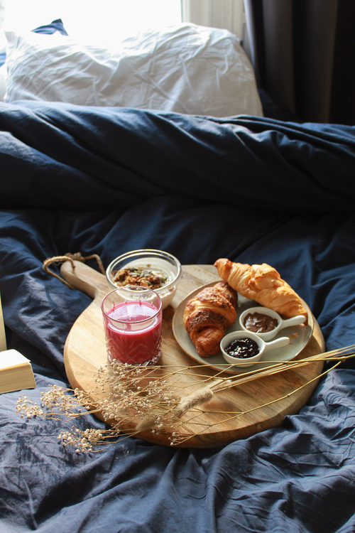 Free A cozy morning in bed with croissants, yogurt, and a smoothie on a wooden board. Stock Photo