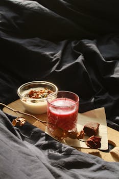 A cozy breakfast setting featuring a bowl of yogurt with granola and a glass of berry juice on a wooden board.