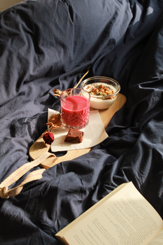 A warm breakfast in bed featuring granola and juice on a wooden board.