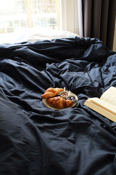 A relaxing morning scene with croissants, dips, and an open book on a bed.