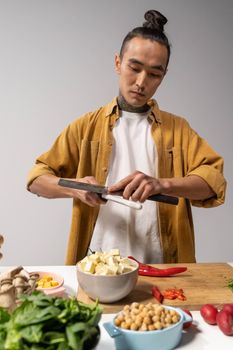 Asian man sharpening knife while cooking with fresh ingredients on the counter.