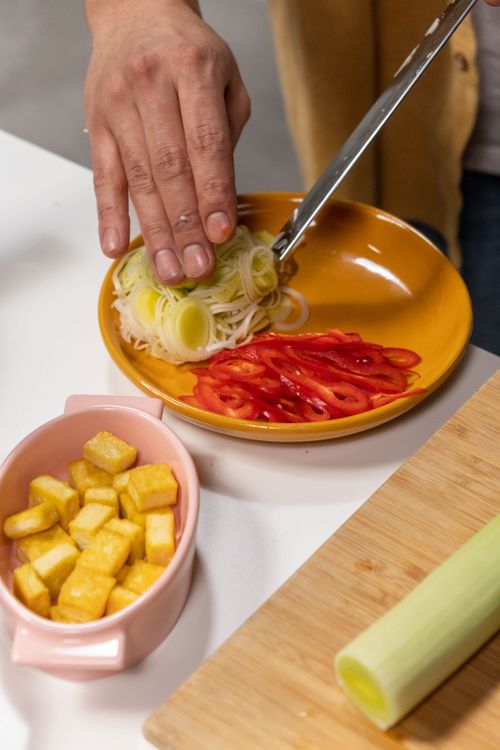 Free Hand prepping sliced vegetables and tofu on a wooden board, showcasing culinary preparation. Stock Photo