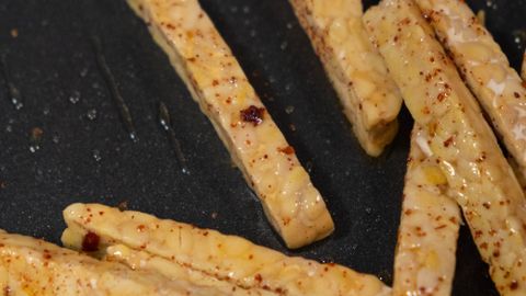 Deliciously seasoned tempeh strips frying to perfection in a nonstick pan.