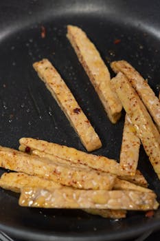 Deliciously seasoned tempeh strips frying to perfection in a nonstick pan.