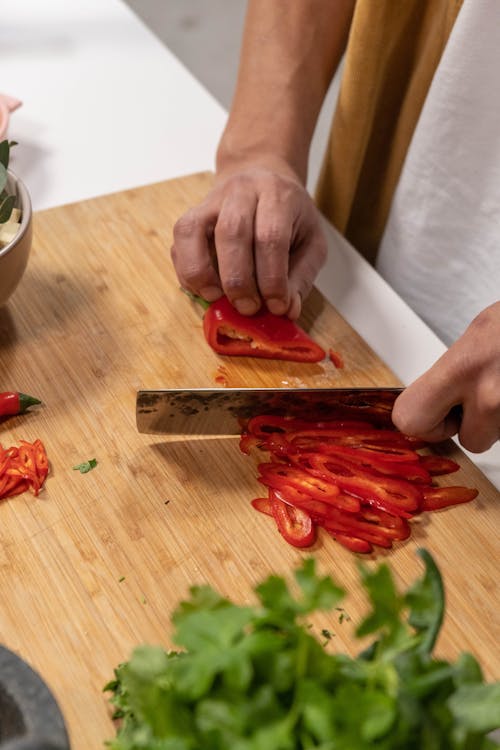 A Person Cutting a Red Bell Pepper on a Chopping Board