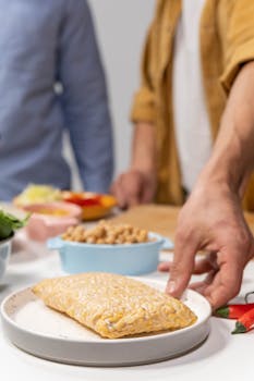 A close-up shot of tempeh on a plate, with hands preparing ingredients in the background.