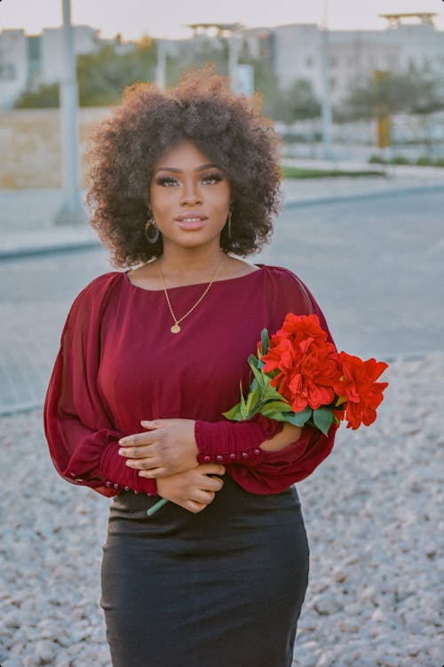 Woman in Red Long Sleeves Carrying Red Flowers on her Arm 