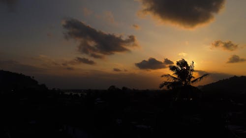 Silhouettes of mountains and palm trees against picturesque cloudy sunset sky in tropical resort