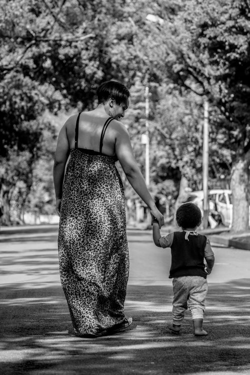 Free A touching black and white photo of a mother walking with her child down a tree-lined street. Stock Photo