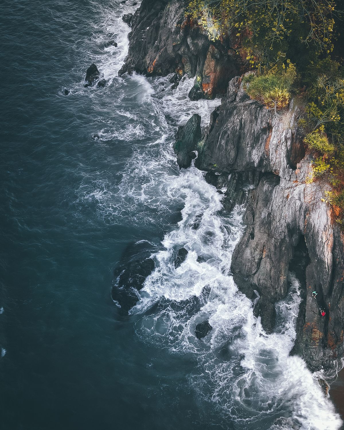 Drone view of powerful turquoise ocean waves crashing against a dramatic rocky coastline