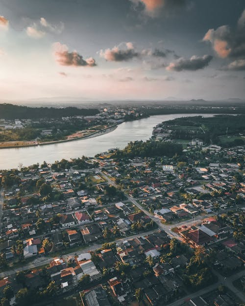 Picturesque drone view of residential houses in small town near river against cloudy sunset sky