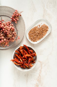 Flat lay of dried chilies, cumin, and pink peppercorns on ceramic plates.