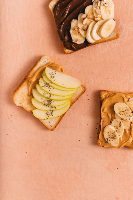 Sliced green and red apples fanned out on a plate with a bowl of peanut butter and a drizzle of honey, sprinkled with granola and chocolate chips.