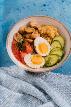 A delicious bowl of quinoa with mushrooms, tomatoes, cucumbers, and boiled eggs on a blue background.