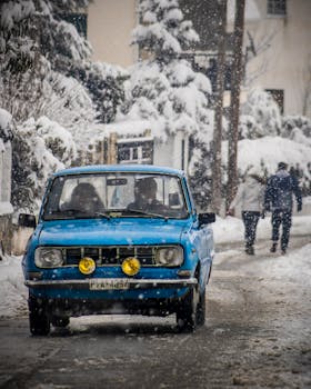Classic blue car drives through a snowy street in Elassona, Greece, capturing winter elegance.