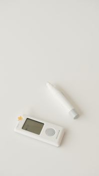 A digital glucometer and pen set against a minimalist white backdrop, symbolizing health monitoring.