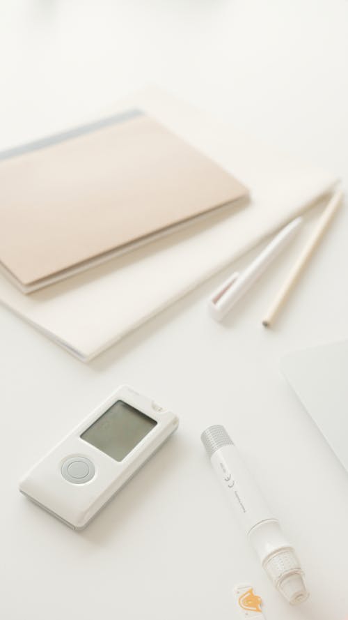 Glucometer and Lancet Pen on White Surface