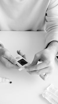 A person using a glucometer to monitor blood sugar levels in black and white.
