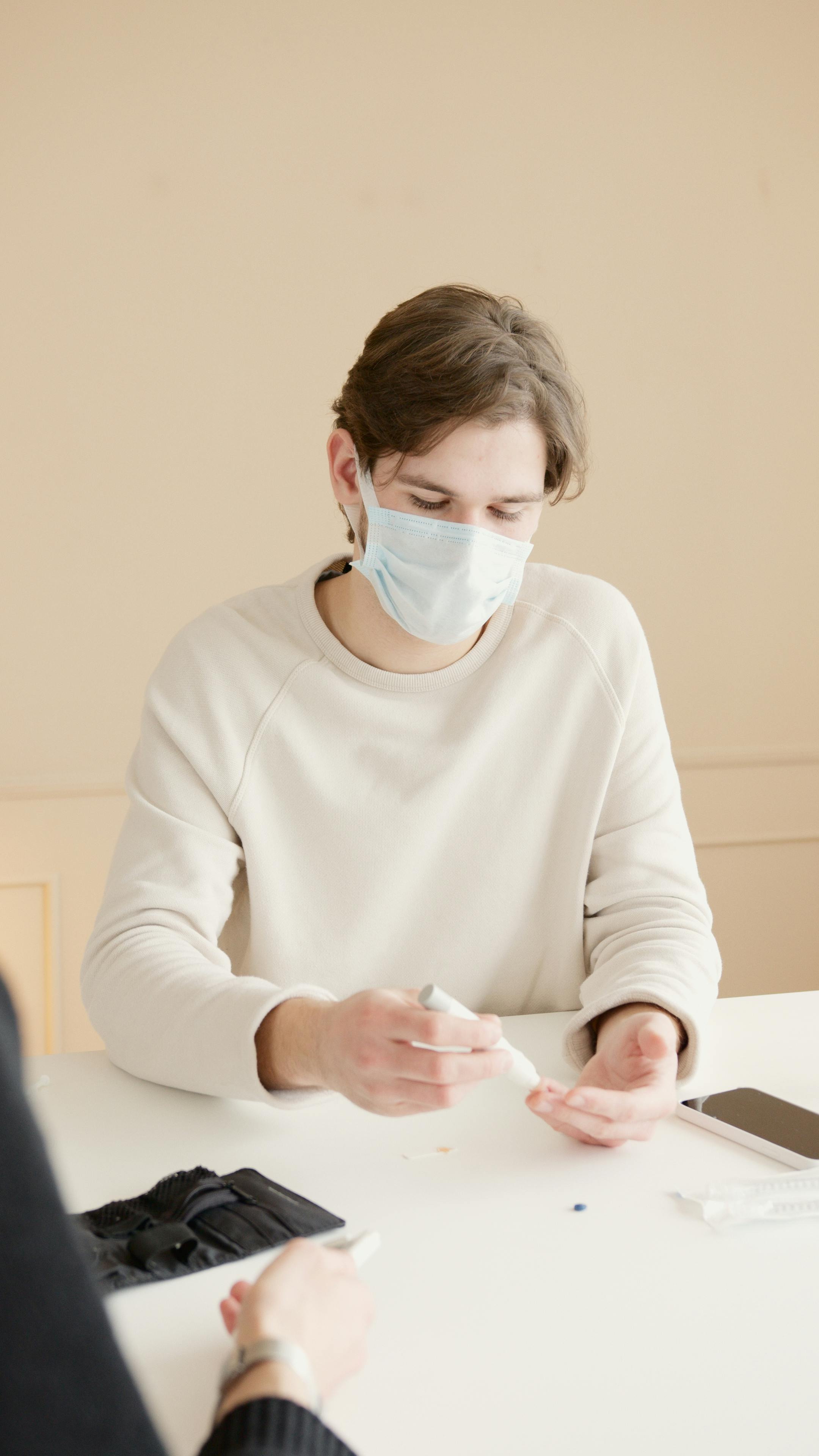 A young man in a face mask handling medical equipment at a white table, exemplifying new normal practices.