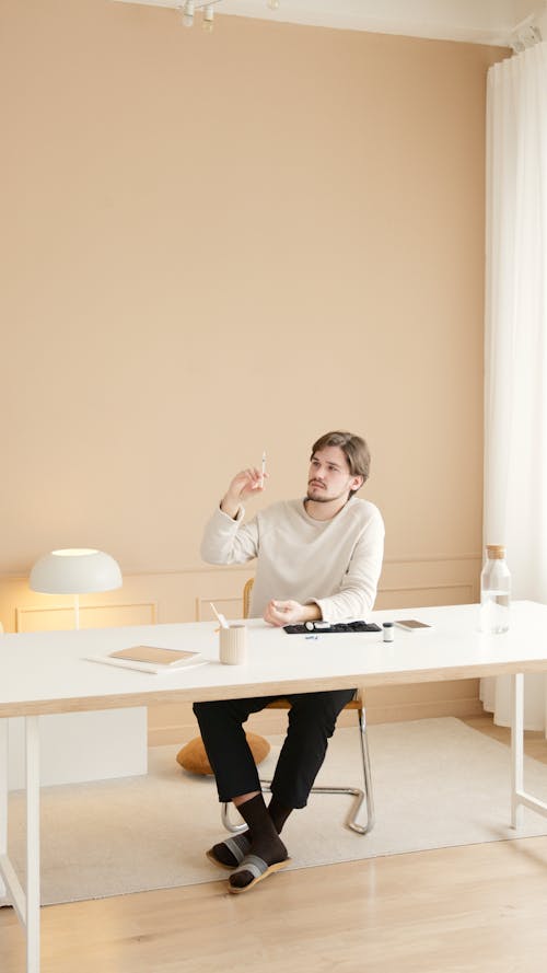 Man in White Sweater Sitting by the Table Holding a Lancet Pen