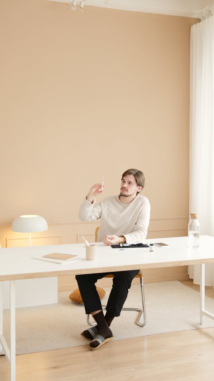 Man In White Sweater Sitting By The Table Holding A Lancet Pen