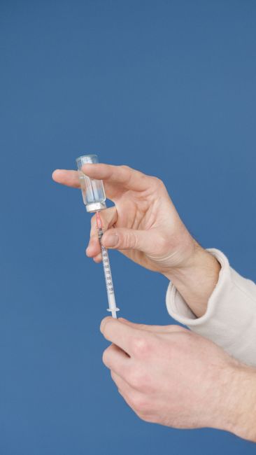 Close-up of hands filling a syringe with a vaccine from a vial against a blue background. Close-up of hands filling a syringe with a vaccine from a vial against a blue background.