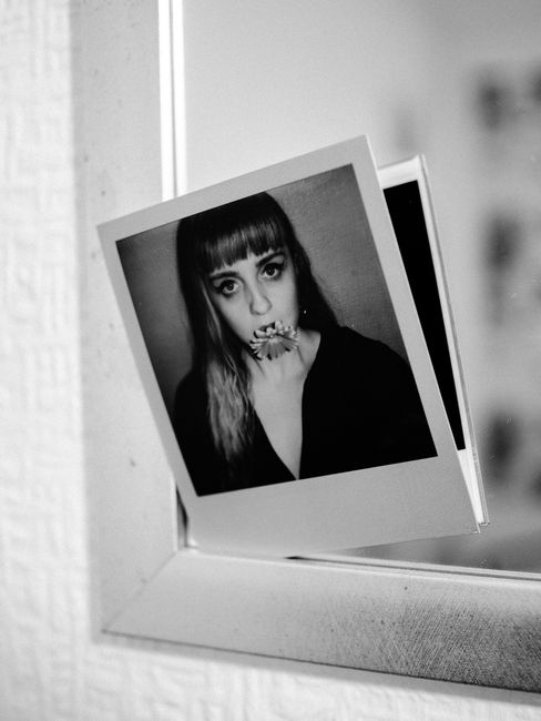Black and white of mirror with instant photography of young female with blossoming flower looking at camera