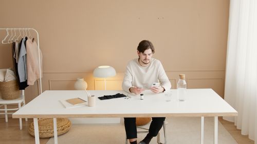 Free A young man using a smartphone while sitting at a minimalist home office table with a stylish decor. Stock Photo